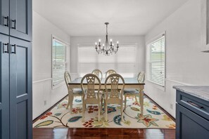 Une salle à manger avec une table, des chaises, un lustre et un tapis à motifs floraux.