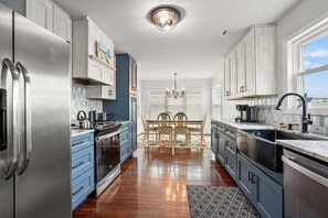 Eine Küche mit einem Edelstahl-Kühlschrank, blauen Schränken, einem Esstisch mit Stühlen und einer Kristallleuchtre.