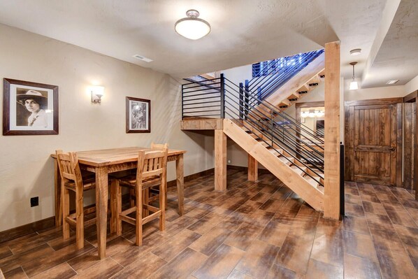 Una mesa de comedor de madera con sillas, una escalera con barandillas de metal y cuadros en la pared.