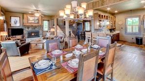 A spacious living area with a fireplace, dining table set for six, and a staircase leading to upper levels.
