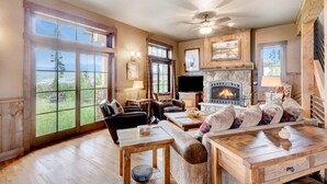 A cozy living room with a fireplace, large windows, and a television.