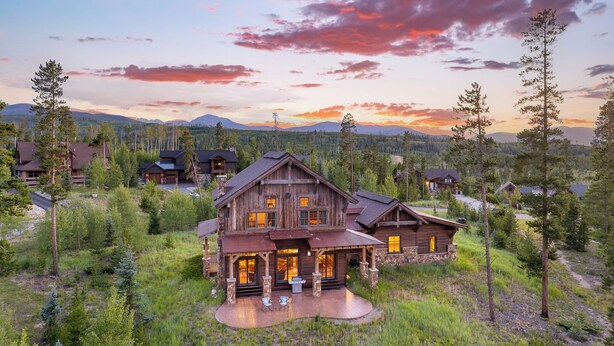 A large wooden cabin with a stone foundation, multiple windows, and a covered patio area.