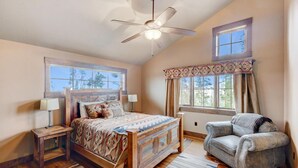 A bedroom with a large bed, a chair, a ceiling fan, and a window with curtains.