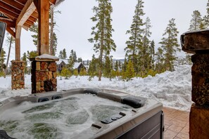 A hot tub with stone pillars, surrounded by snow and trees.