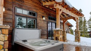 A wooden cabin with a stone exterior, a hot tub, and a covered porch.