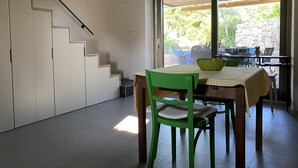 Un comedor con una mesa dispuesta para dos, una silla verde y vistas a un patio exterior con un muro de piedra y vegetación.