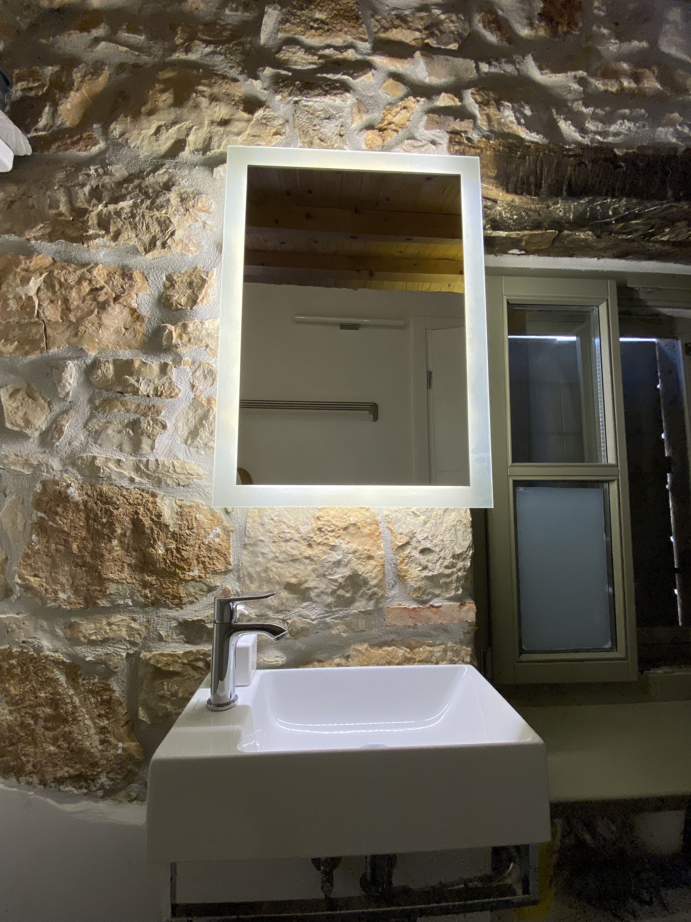 Un baño con pared de piedra, un lavamanos blanco y un espejo.