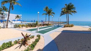 Un paseo marítimo frente a la playa, con palmeras, un paseo peatonal y vistas al océano.