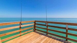 Un muelle de madera con dos cañas de pescar que se adentran en el mar bajo un cielo azul despejado.
