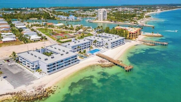 Un resort con varias construcciones, una playa y aguas cristalinas.