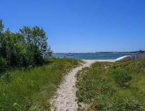 A sandy path leading to a beach with a clear blue sky.