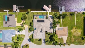 An aerial view of a property with a swimming pool, a tennis court, and a large lawn area.