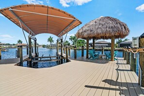 Eine Holzterrasse mit Pool, einem strohgedeckten Gebäude und Sitzgelegenheiten im Freien.