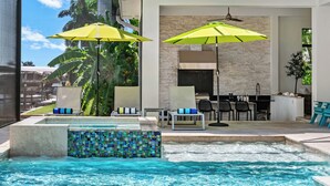 Un área de piscina con jacuzzi, sillones de descanso y sombrillas.