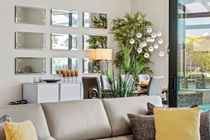 Una sala moderna con un sofá, una mesa de comedor con sillas, una planta grande en maceta y varios espejos colgados en la pared.