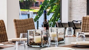Una mesa de comedor con sillas de mimbre, copas de cristal transparente y una botella de vino.
