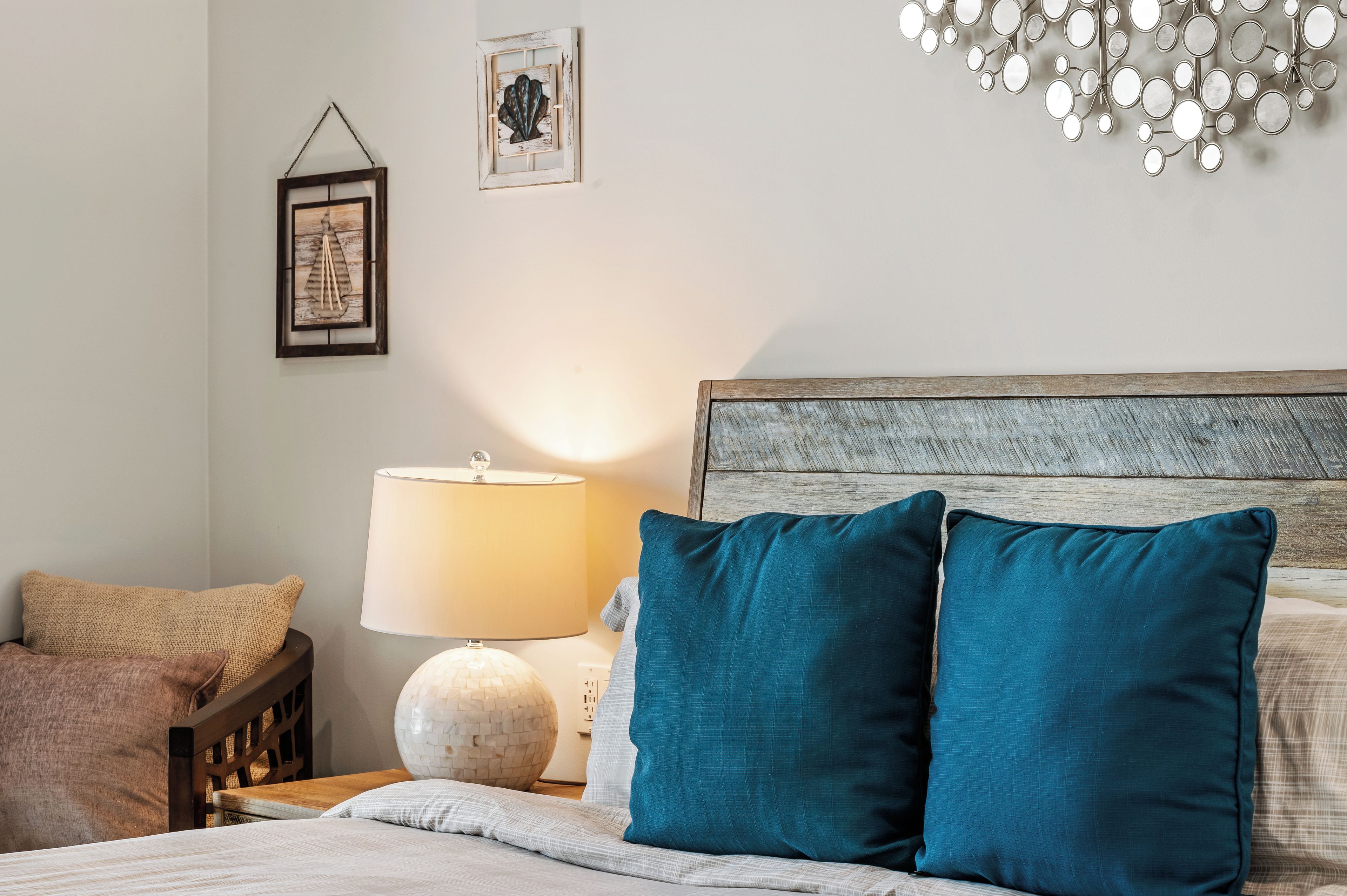 Ein ordentlich bezogenes Bett mit zwei türkisfarbenen Kissen, einem Holzkopfteil, einer Nachttischlampe und einem Wanddekor.