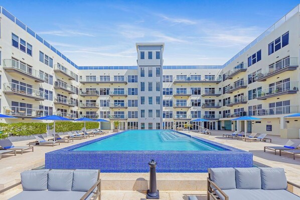 A modern hotel with a central swimming pool surrounded by lounge areas and multiple balconies. - Studio Head-turning Style & Extraordinary Location (Oranjestad)