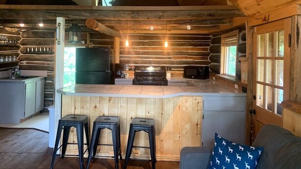 Interior rústico de una cabaña con una zona de bar de madera, una kitchenette y un rincón de estar acogedor.