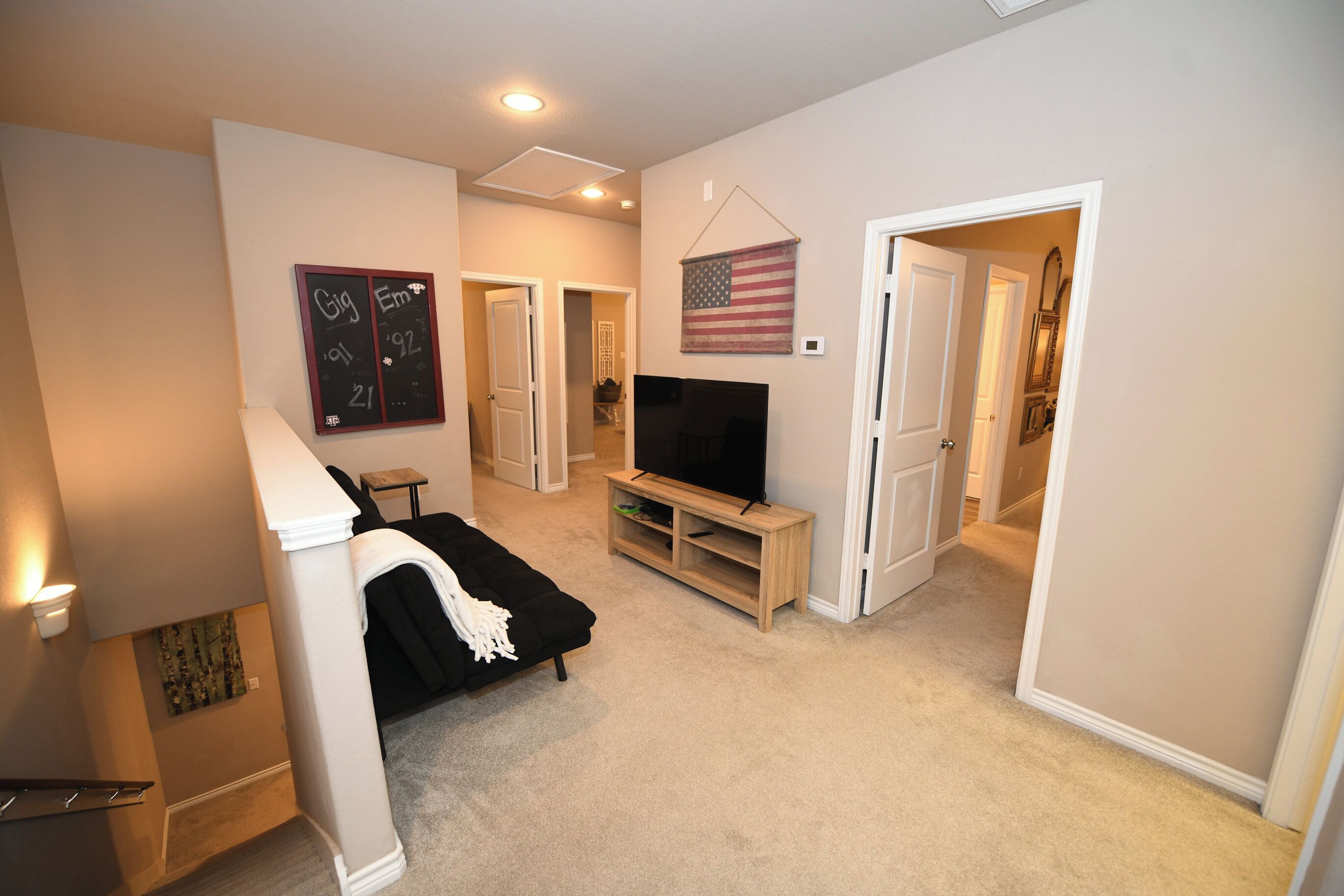 A bedroom with a bed, a TV on a wooden stand, a wall-mounted American flag, and a chalkboard with writing.