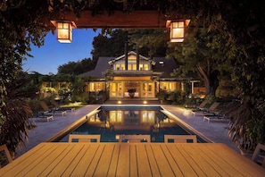 A large house with a swimming pool, surrounded by trees and outdoor furniture.