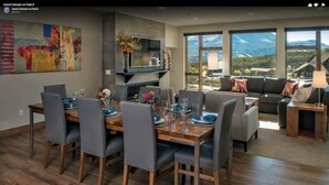 A modern dining area with a wooden table and chairs, a fireplace, and a large window offering a mountain view. - Ski In - Ski Out, Two-Bedroom Breckenridge Residence on Peak 8, Corner unit (Breckenridge)