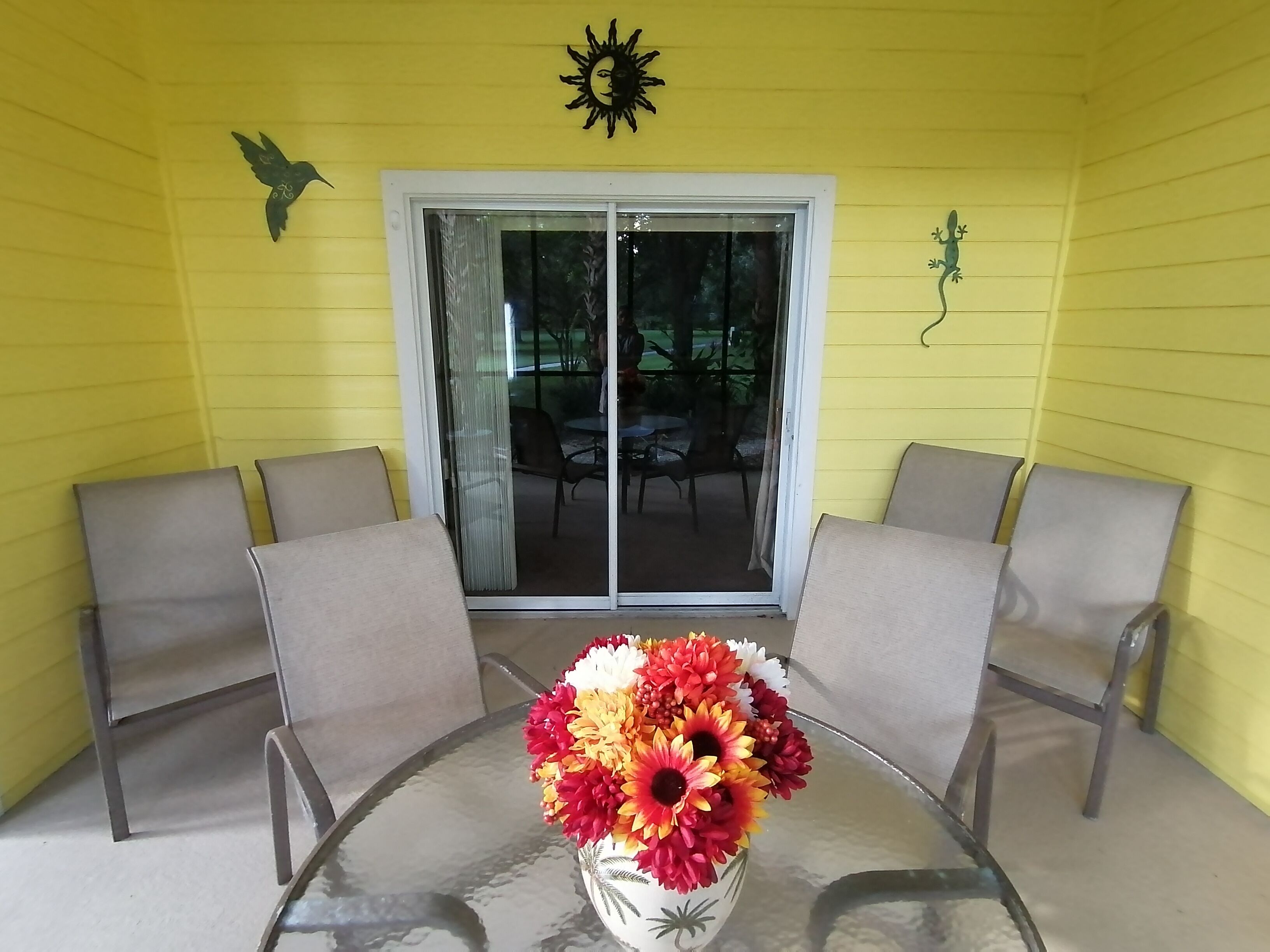 Une pièce jaune avec une table et des chaises en verre, un vase de fleurs et une porte-fenêtre coulissante donnant sur l’extérieur.