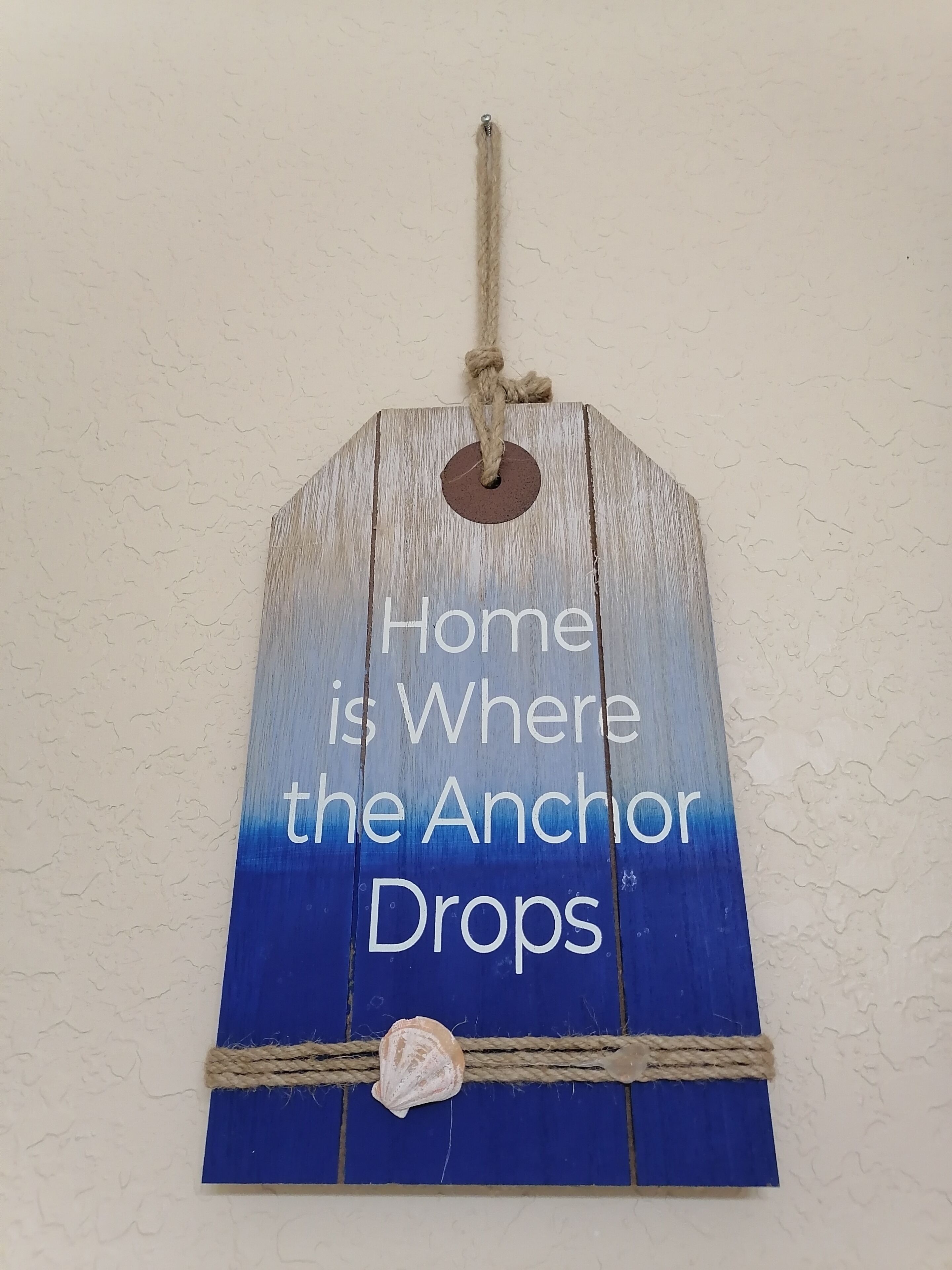 A wooden sign with the text "Home is Where the Anchor Drops" and a rope tied around it.