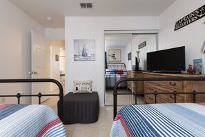 Un dormitorio con dos camas, un televisor y un cuadro de veleros.
