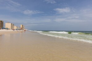 Ein Strand mit sandigem Ufer, Wellen und Gebäuden im Hintergrund.