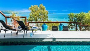 Ein Poolbereich mit Liegestühlen, einer Holzterrasse und Blick aufs Meer.