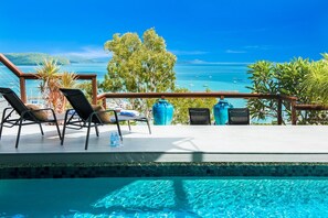 A pool area with lounge chairs, a wooden deck, and a view of the sea. - Airlie Beach Seaviews (Airlie Beach)