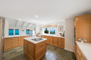A spacious kitchen with wooden cabinets, a central island, and large windows offering a view of the ocean. - Airlie Beach Seaviews (Airlie Beach)