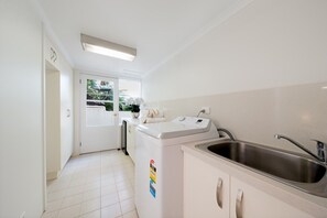 A compact kitchen with a built-in washing machine, a stainless steel sink, and a window with a view of greenery. - Airlie Beach Seaviews (Airlie Beach)