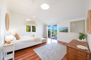 A bedroom with a bed, bedside table, lamp, and a view of the outdoors through a sliding door. - Airlie Beach Seaviews (Airlie Beach)
