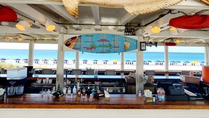 A seafood restaurant with a large fish hanging above the bar, a menu board, and a view of the beach. - Pet-Friendly Maravilla Condo–Beach Ramp, Pools, Free Beach Setup, 1BDR + Bunks (Miramar Beach)