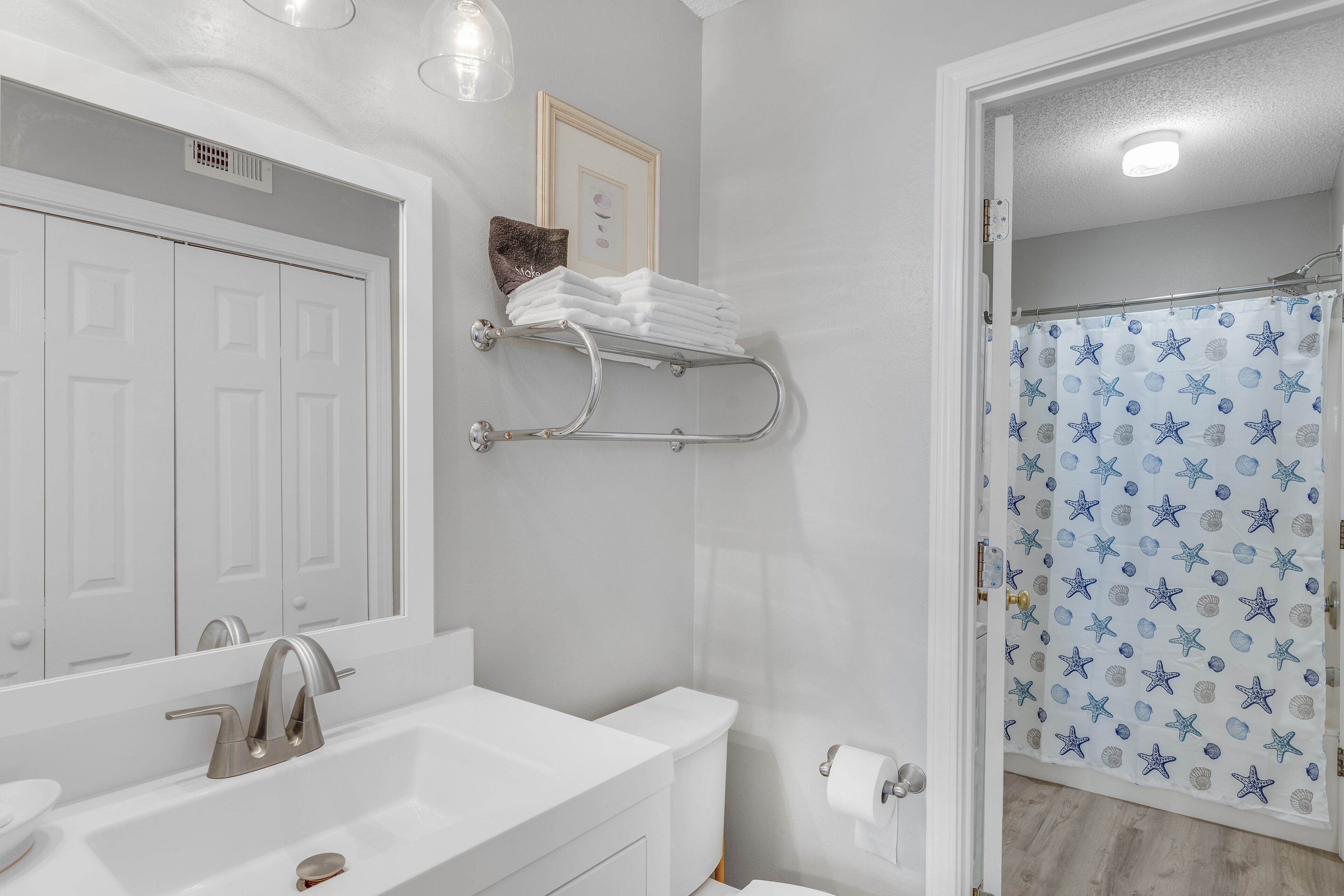 Un baño con un lavamanos blanco, un inodoro, una cortina de ducha con estampado de estrellas y un perchero con toallas dobladas.