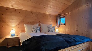 A wooden cabin bedroom with a bed, pillows, and bedside lamps. - Vacation home with conservatory, fireplace and garden barbecue in a secluded location in the mountains (Tschagguns)
