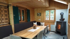 A cozy wooden cabin with a dining table, chairs, a fireplace, and a window with a view of trees. - Vacation home with conservatory, fireplace and garden barbecue in a secluded location in the mountains (Tschagguns)