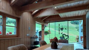 A wooden interior with a dining table, chairs, and a view of a green landscape through large windows. - Vacation home with conservatory, fireplace and garden barbecue in a secluded location in the mountains (Tschagguns)