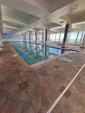 Una piscina interior con suelo de baldosas hexagonales, agua cristalina y vistas al exterior a través de amplios ventanales.