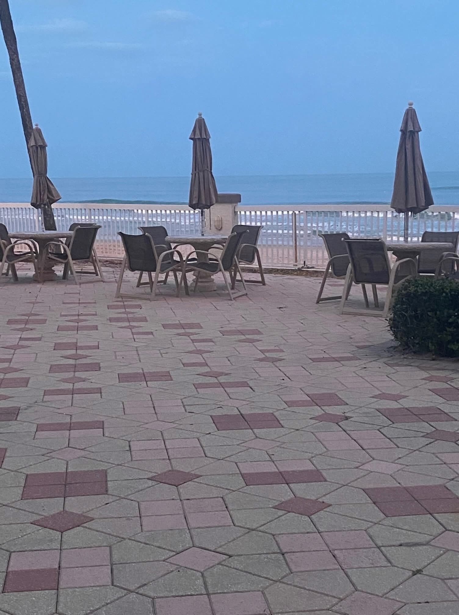 An outdoor seating area with hexagonal patterned tiles, chairs, and umbrellas, overlooking a body of water.