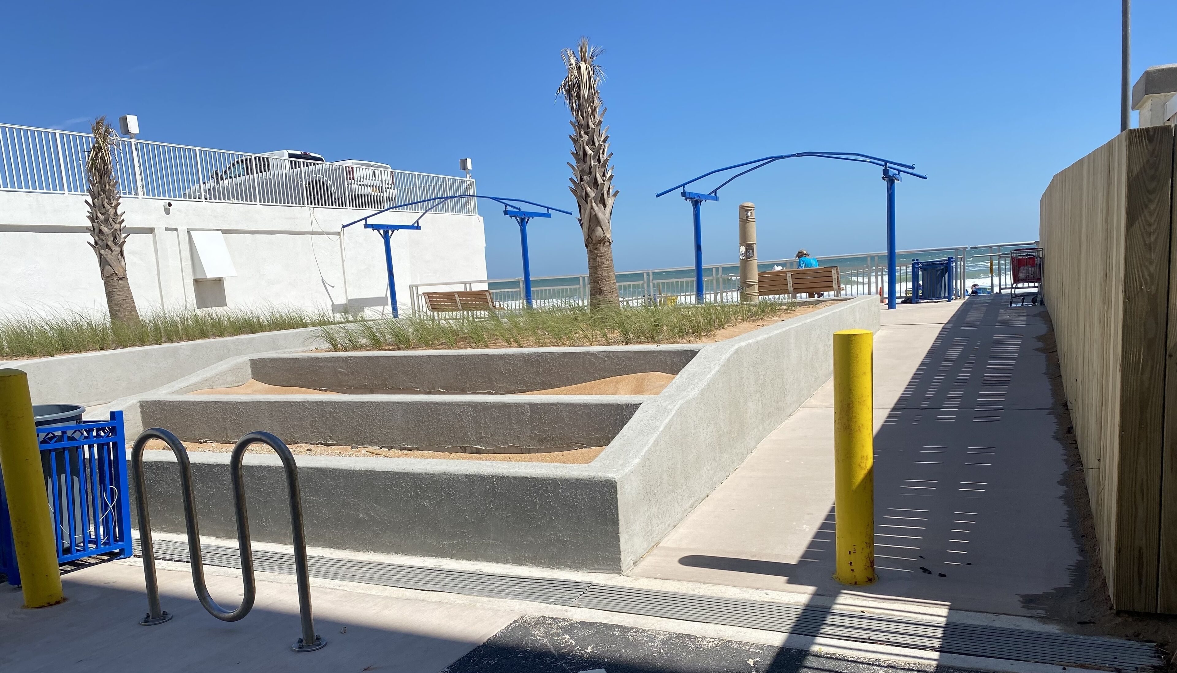 A coastal walkway with a concrete planter, metal railings, and a bench.