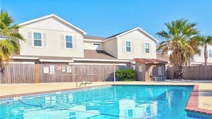 Une piscine avec une terrasse en bois, une clôture en bois et deux maisons en arrière-plan.