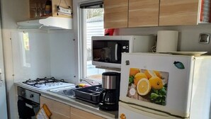 Una cucina compatta con piano cottura a gas, microonde e frigorifero bianco decorato con calamite a forma di frutta.