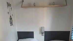 Camera d'albergo con due letti singoli, un comodino, una mensola a parete con soprammobili e una decorazione murale.