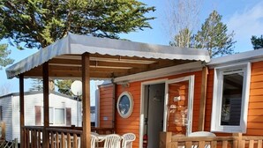 Un patio in legno con tavoli e sedie da picnic, un portico coperto e una porta che conduce a una baita.