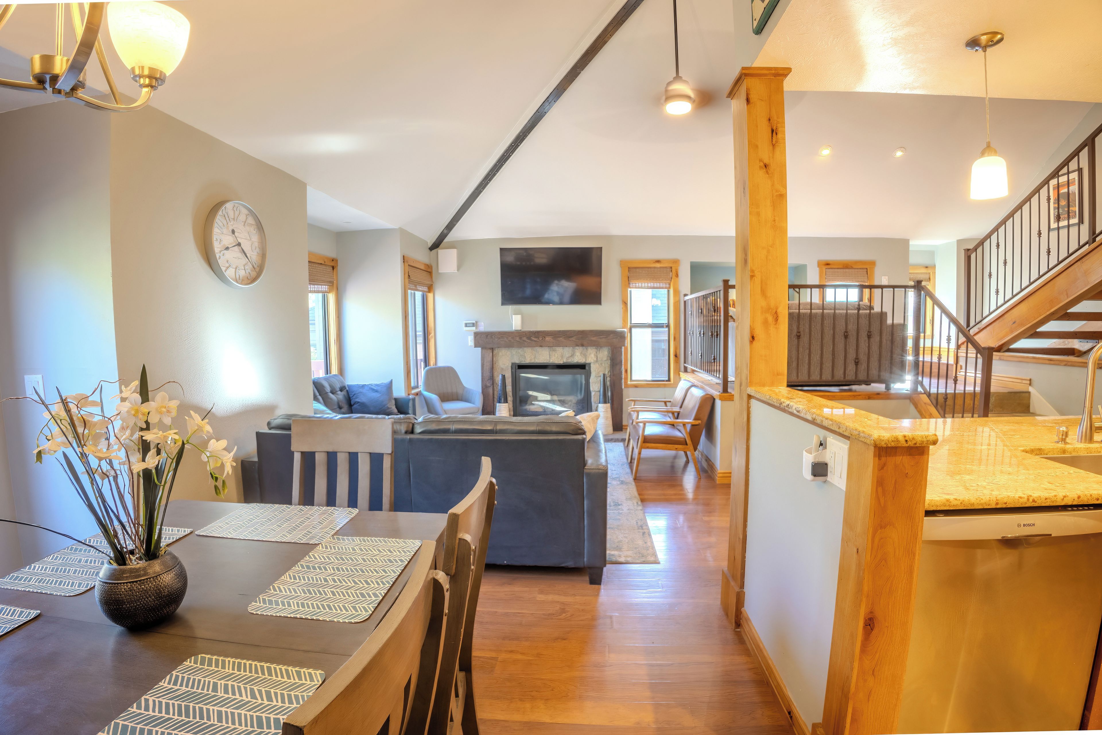 A spacious living area with a fireplace, a dining table with placemats, and a staircase leading to an upper level.