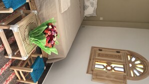 Een kamer met een bed, een houten kist, een raam met een stervormig ontwerp en een bloemenboeket.