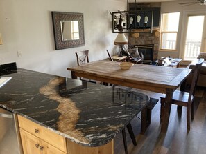 Een keuken met een zwarte marmeren aanrecht, een houten eettafel en stoelen. Er is een stenen open haard en een spiegel aan de muur.